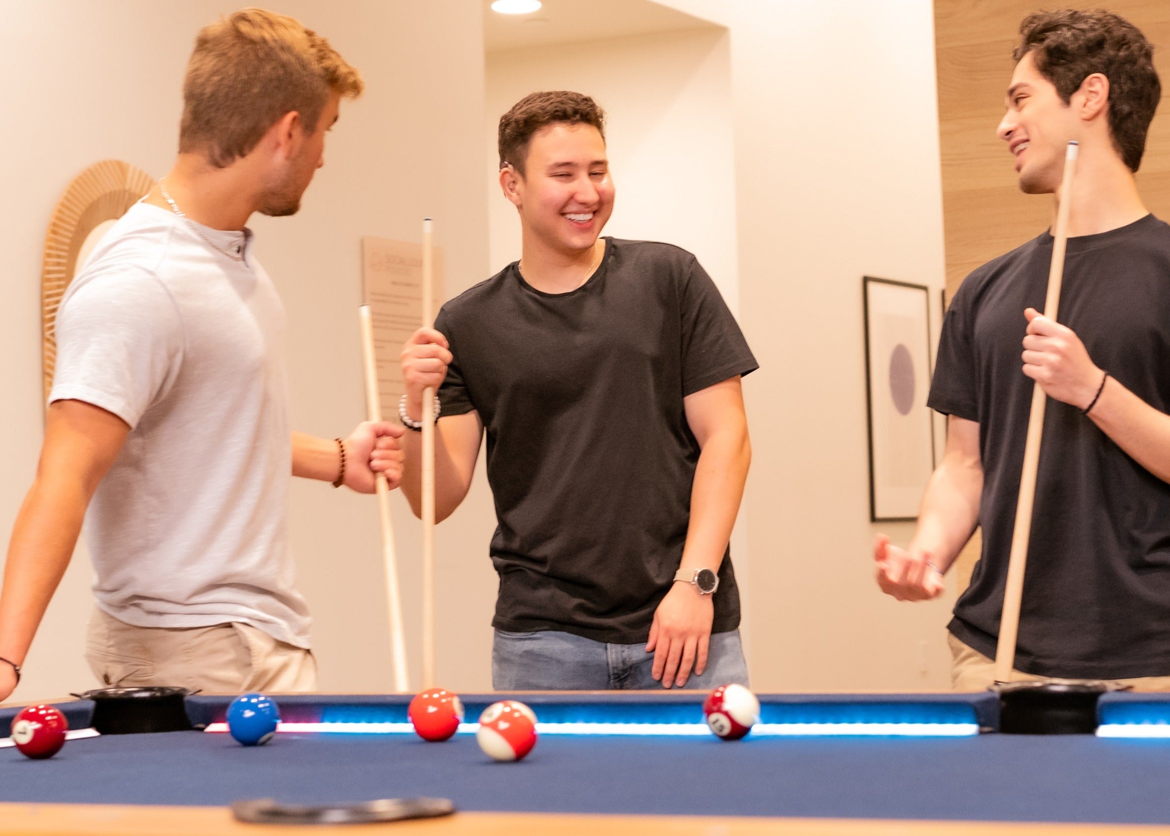 Three men playing pool together in a room with a neutral color scheme.